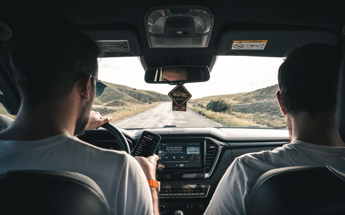 Two men driving through a scenic landscape, using a cellphone for navigation.