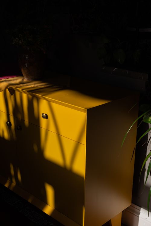Free A dramatic yellow cabinet partially lit with moody shadows in a dark, indoor setting. Stock Photo