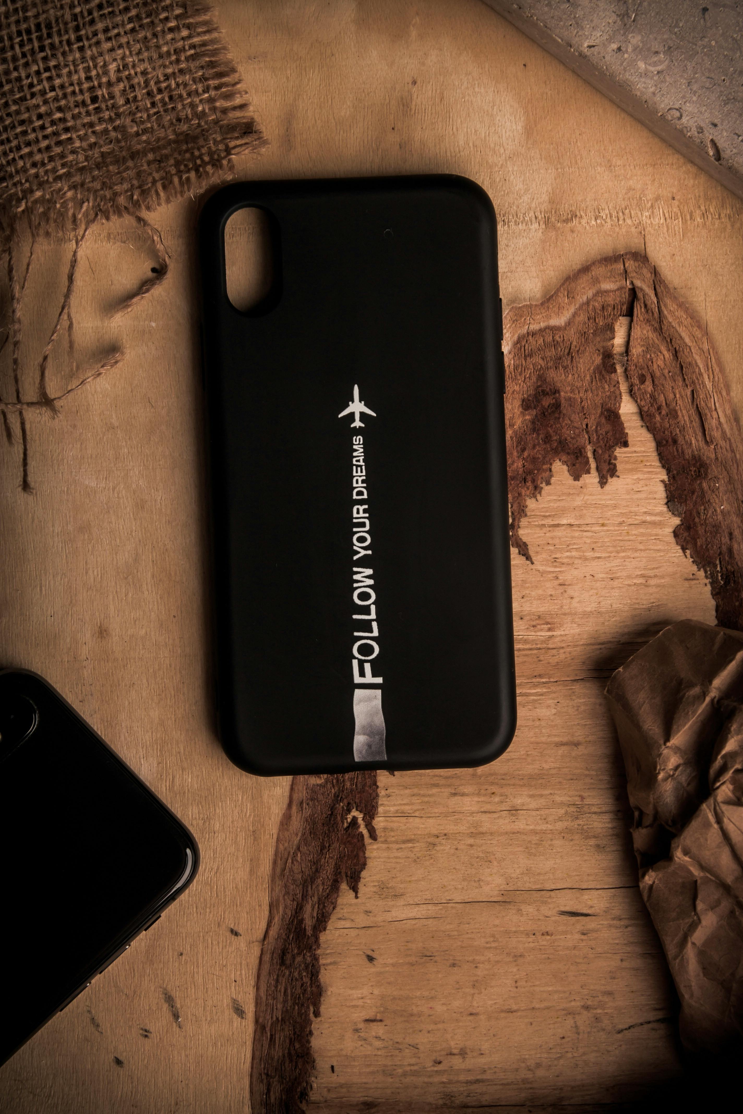 Black phone case with 'Follow Your Dreams' message on rustic wooden table.