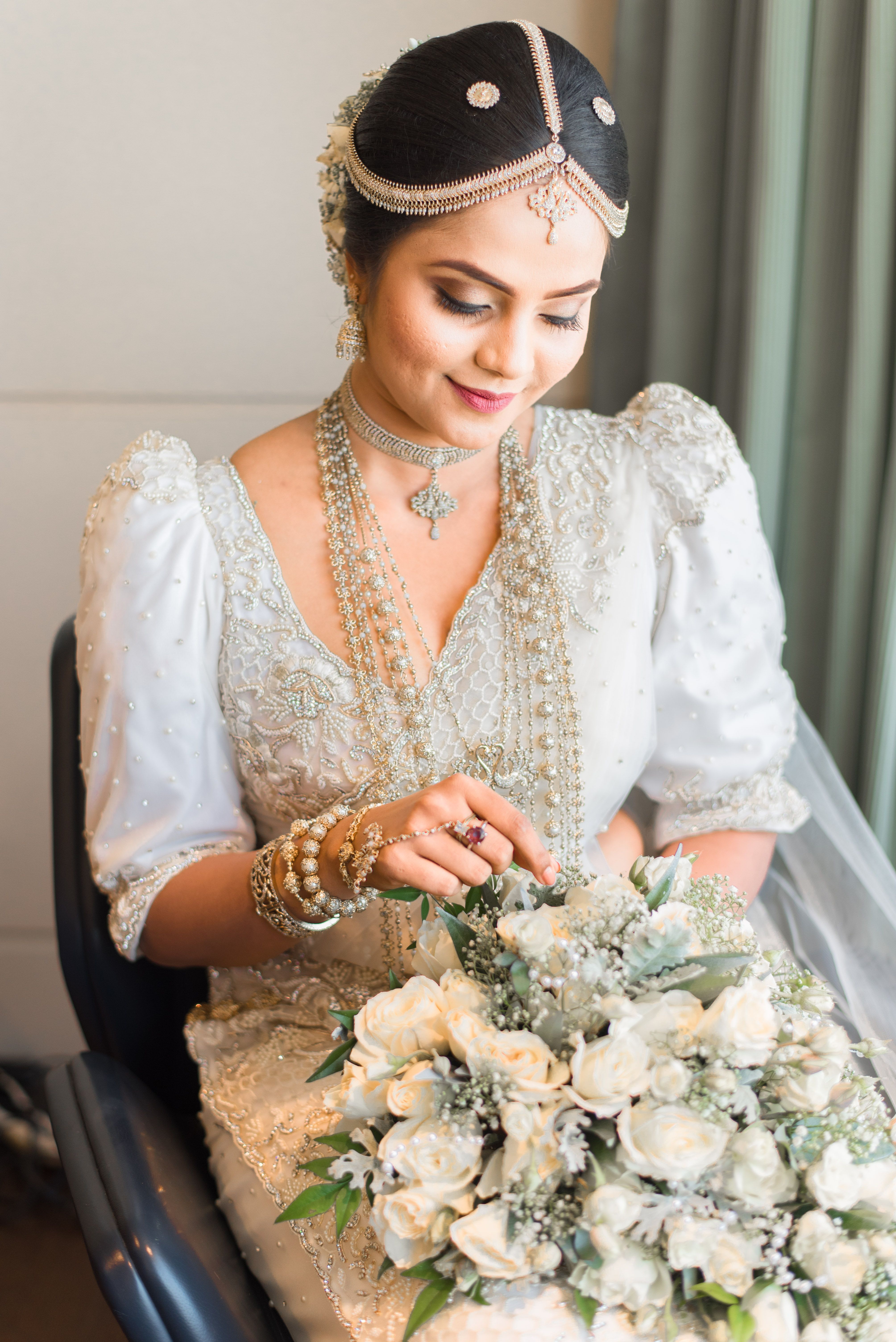 Seated Kandyan bride in embroidered silver saree with rose bouquet