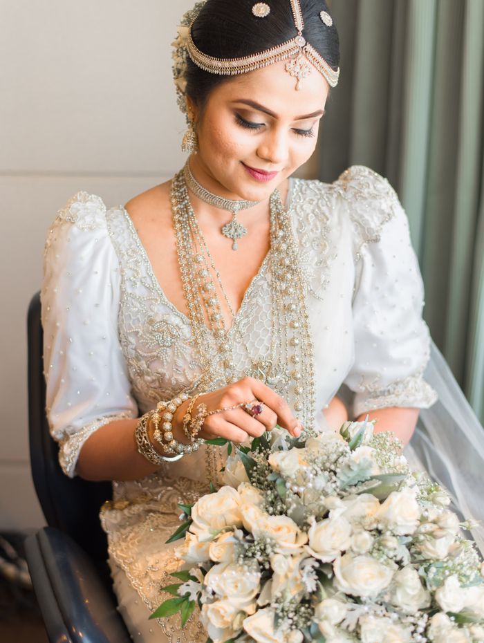 Seated Kandyan bride in embroidered silver saree with rose bouquet