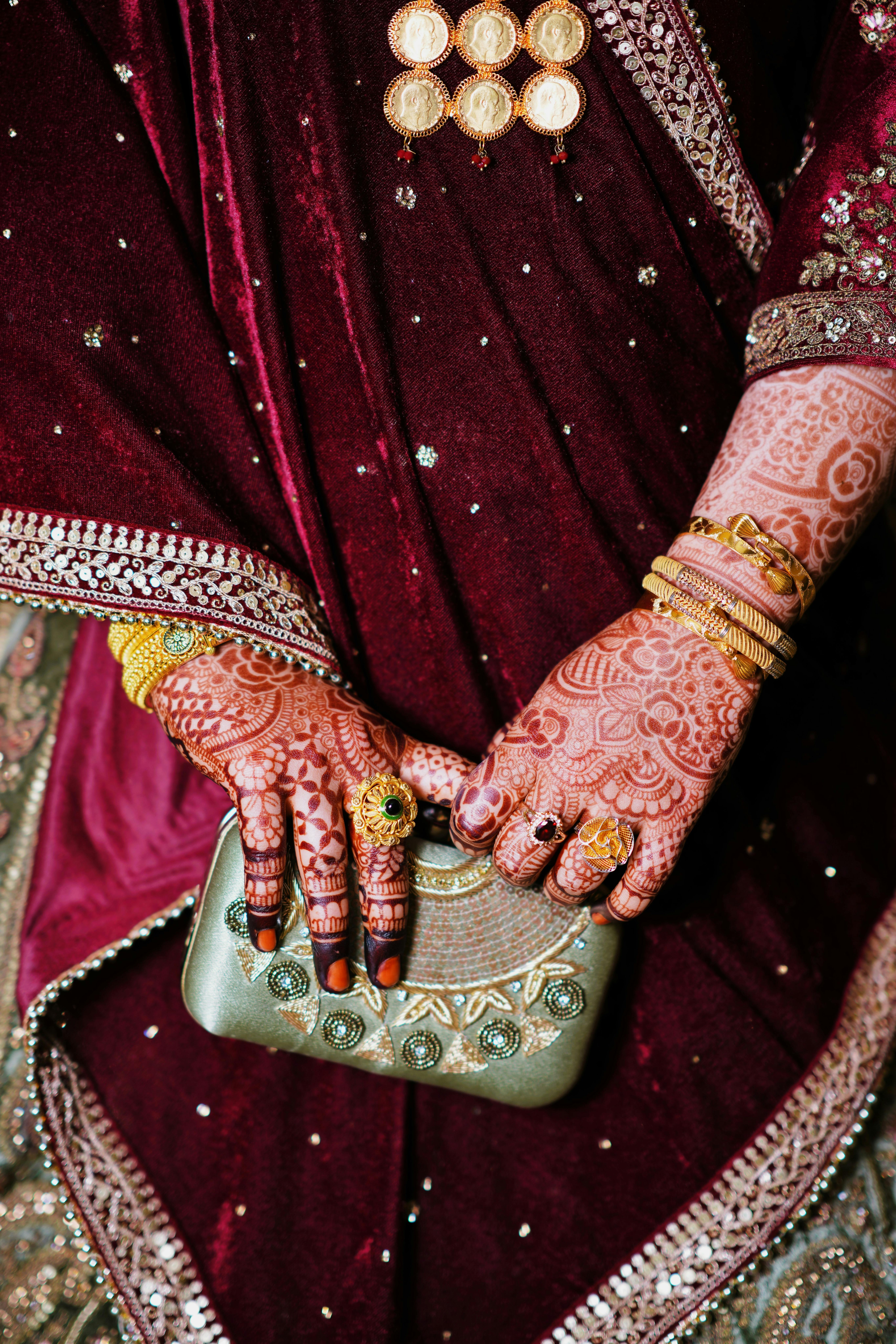 Close-up of henna-adorned hands holding a clutch, showcasing intricate bridal mehendi and traditional jewelry.