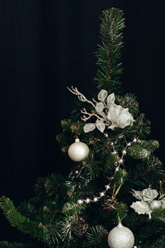 深色背景上，一棵装饰着银色花环、饰品和花卉的圣诞树特写镜头