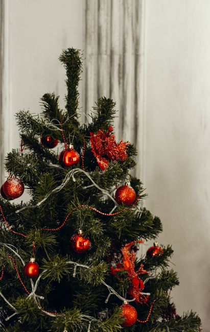 A beautifully decorated Christmas tree with red ornaments and pine garlands indoors.