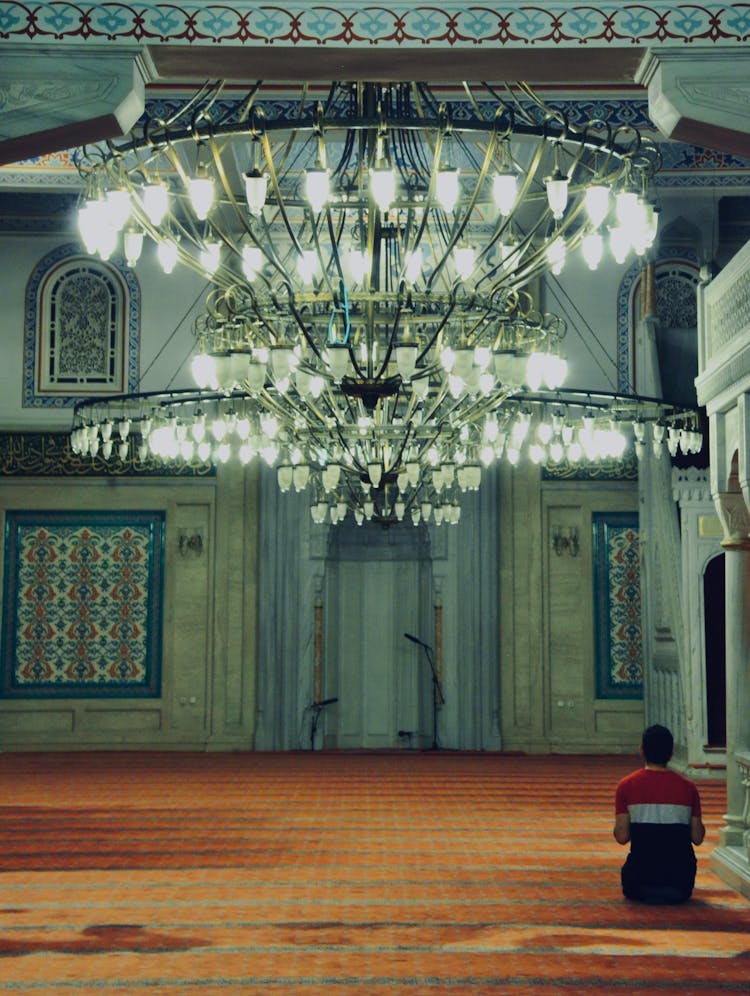 Back View Of A Man Sitting On The Floor And Praying In A Mosque 