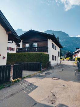 Traditional Bavarian architecture in a quiet street in Garmisch-Partenkirchen, Germany, with mountains in the backdrop.