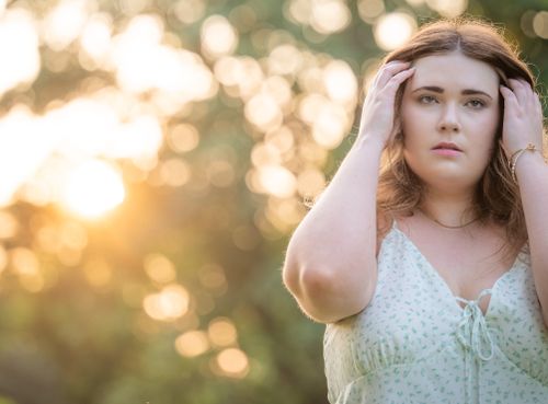 Free A woman in a summer dress poses thoughtfully in a sunlit garden, expressing serenity. Stock Photo
