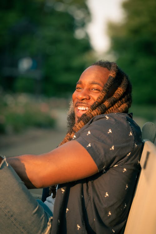 Man with Dreadlocks Sitting on a Bench in a Park and Laughing