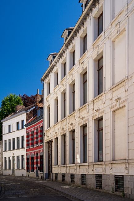 A sunny day on a traditional street lined with colorful old buildings in Mons, Belgium.