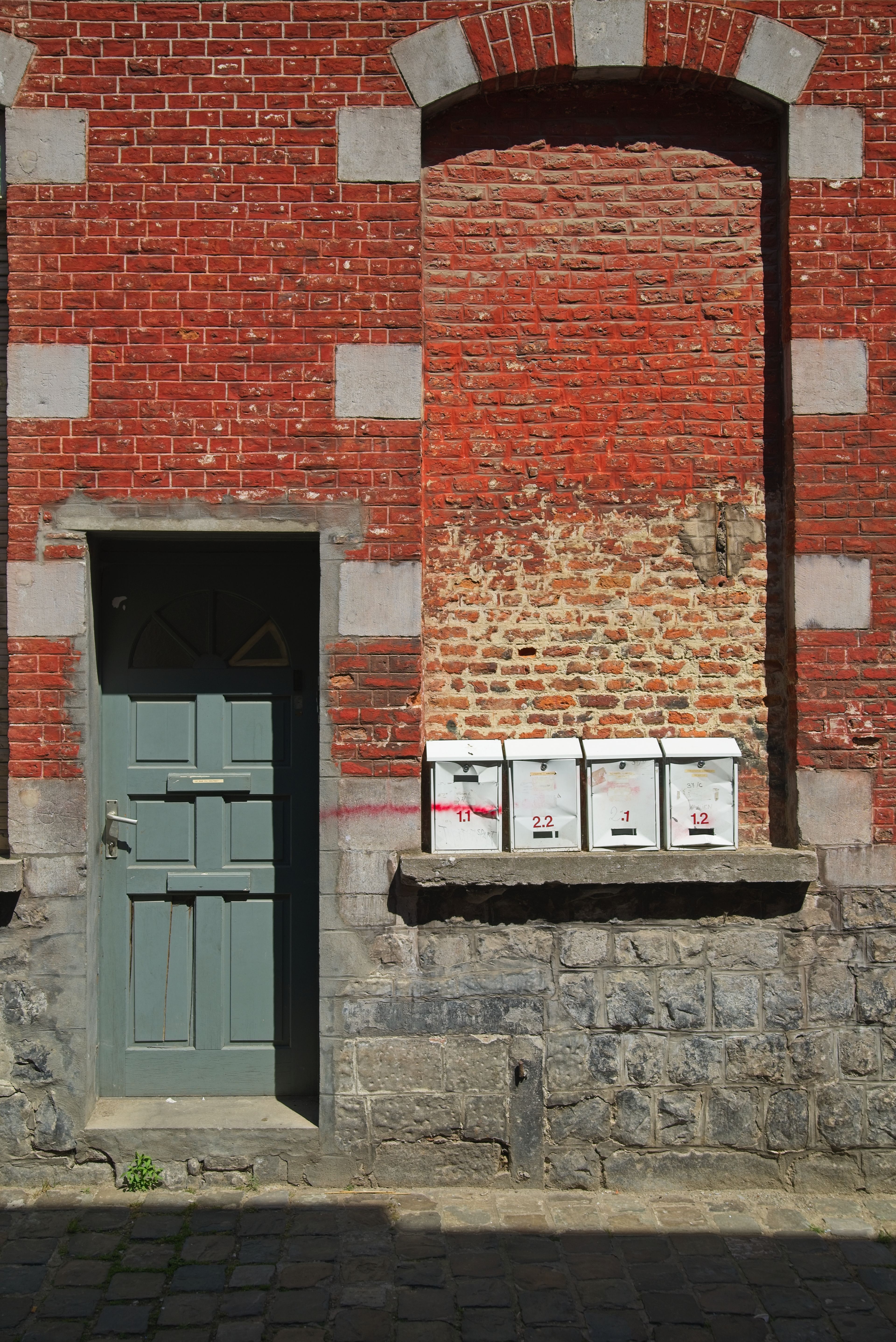 Porte d'entrée d'un immeuble ancien en brique rouge, boîtes aux lettres alignées sur le mur
