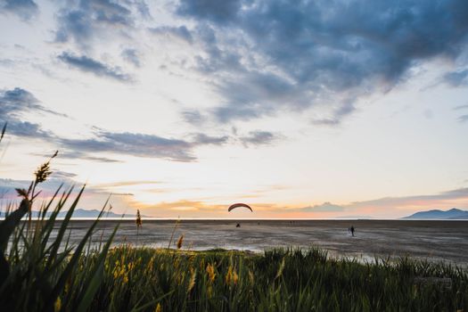 A scenic view of a paraglider over Salt Lake City at twilight with grassy foreground.