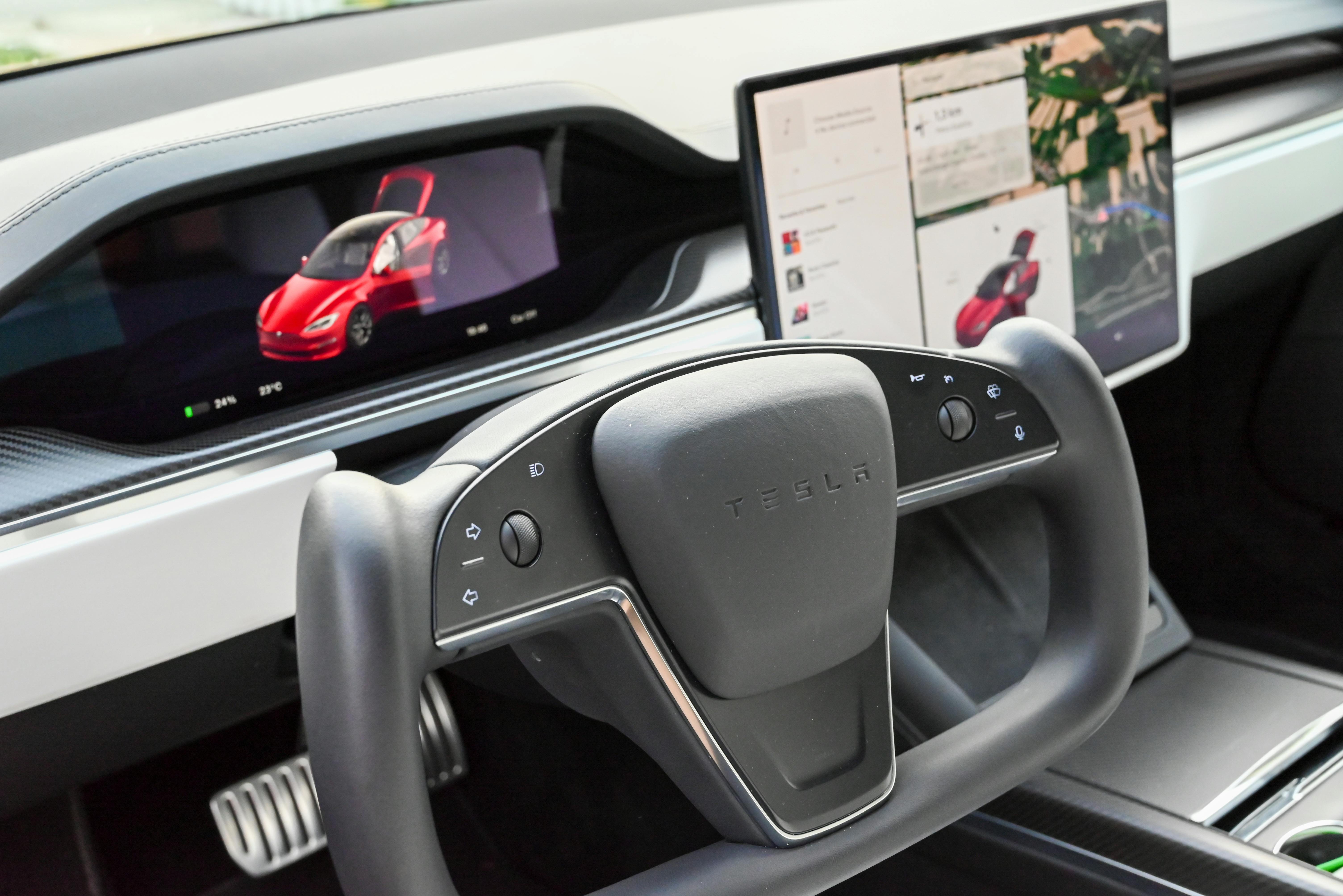 Modern Tesla car interior featuring a steering yoke and digital displays showcasing features.
