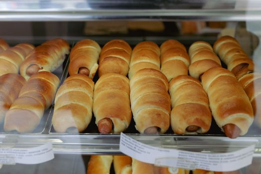 Close-up of freshly baked sausage rolls in a bakery display, showcasing golden brown pastry.