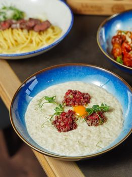 Delicious risotto topped with beef tartare and herbs served in a blue bowl.
