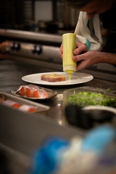 Chef expertly drizzles sauce on a dish, showcasing culinary skills in a professional kitchen.