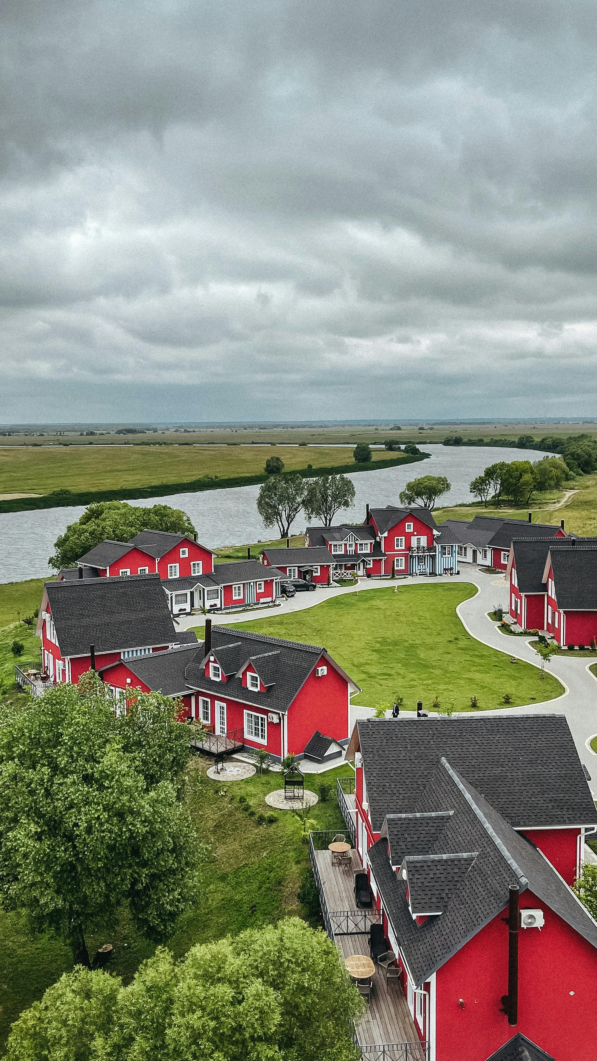 A picturesque aerial view of a red village nestled by a winding river under a cloudy sky.