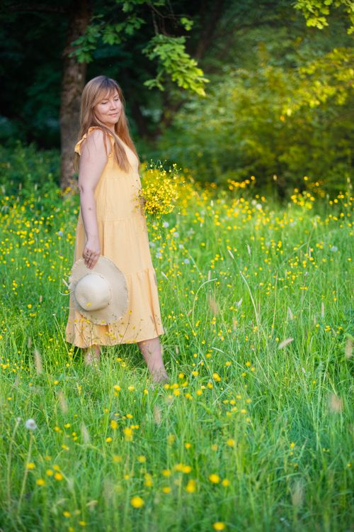 Free Woman in a yellow dress standing in a meadow with flowers, enjoying nature. Stock Photo