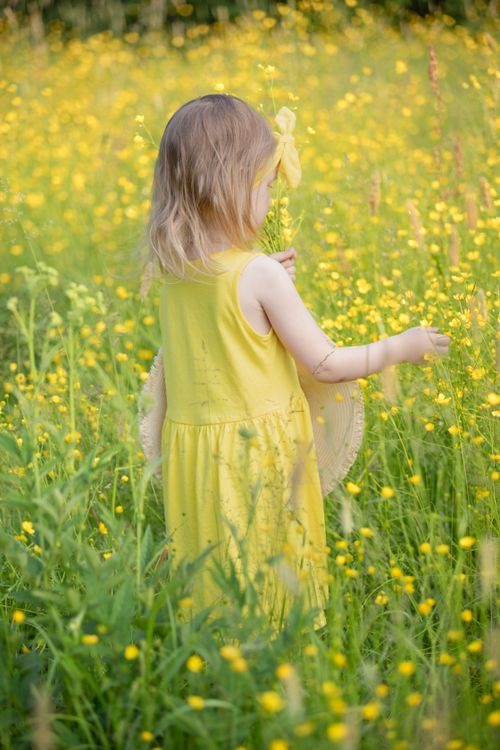 Free A young girl in a yellow dress exploring a vibrant flower-filled meadow on a sunny day. Stock Photo