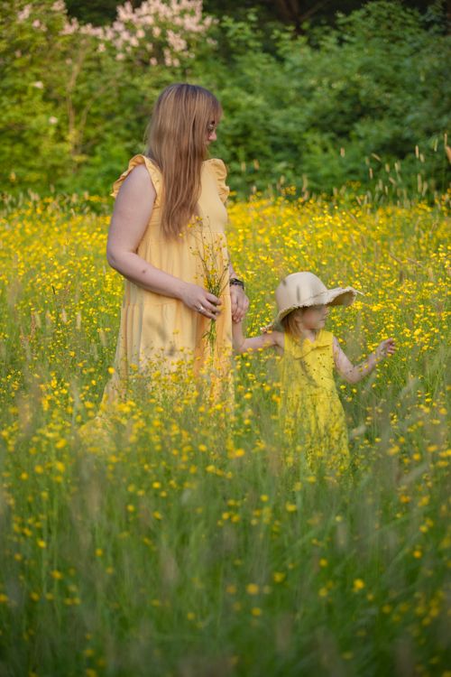 Free A mother and daughter in yellow dresses enjoying a beautiful meadow filled with flowers. Stock Photo