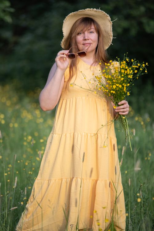 Free A woman in a yellow dress with a hat stands in a meadow holding flowers. Stock Photo