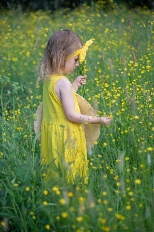 Free Child in a yellow dress standing in a flower-filled meadow, evoking a warm, springtime vibe. Stock Photo