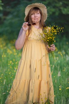 A woman in a yellow dress enjoys a sunny day in a blooming meadow.