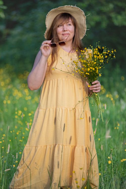 Free A woman in a yellow dress enjoys a sunny day in a blooming meadow. Stock Photo