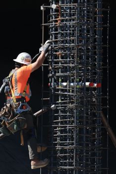 Worker in safety gear climbs a steel scaffolding structure on a construction site under daylight.