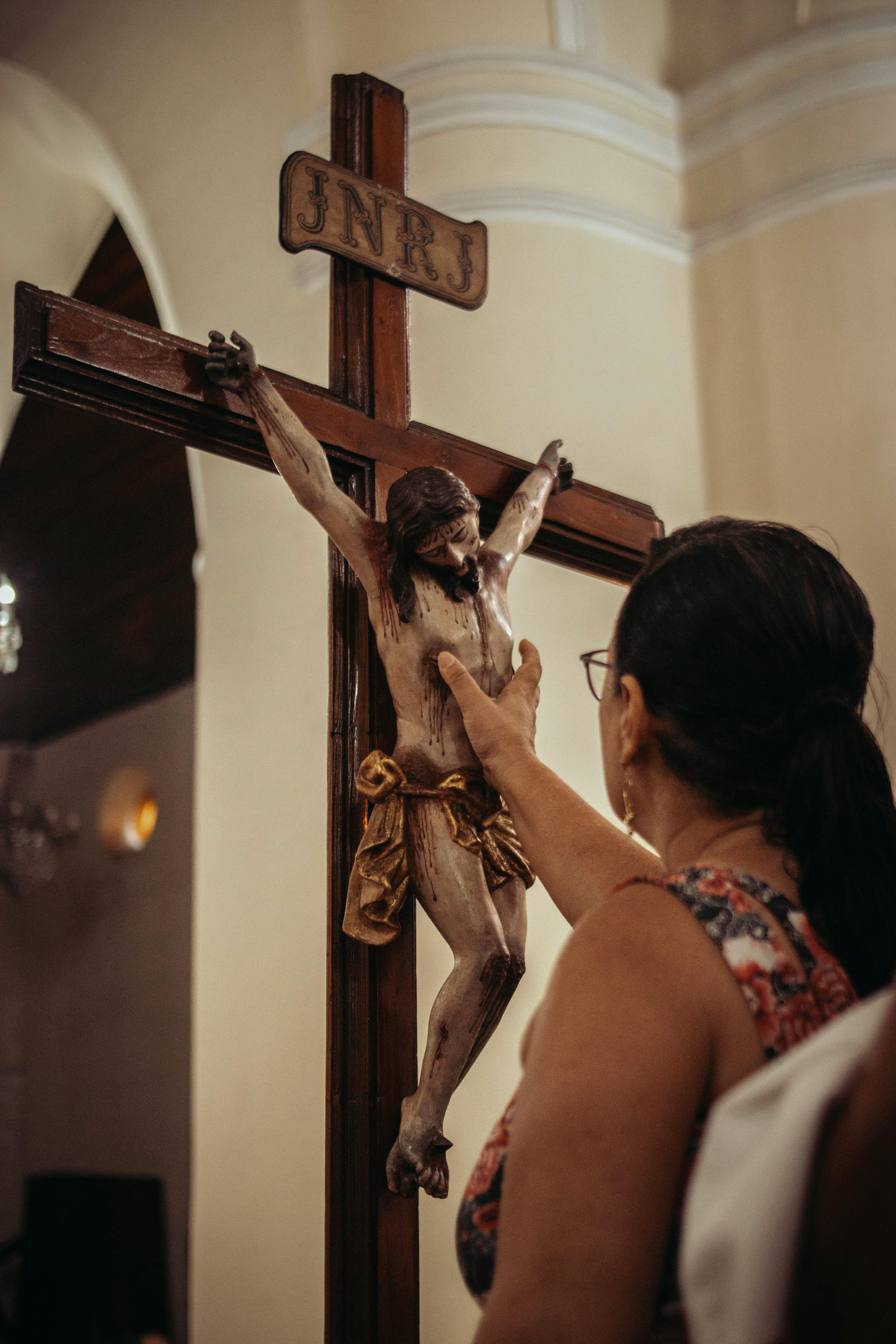 A woman reverently touches a crucifix in a solemn church interior, symbolizing faith.