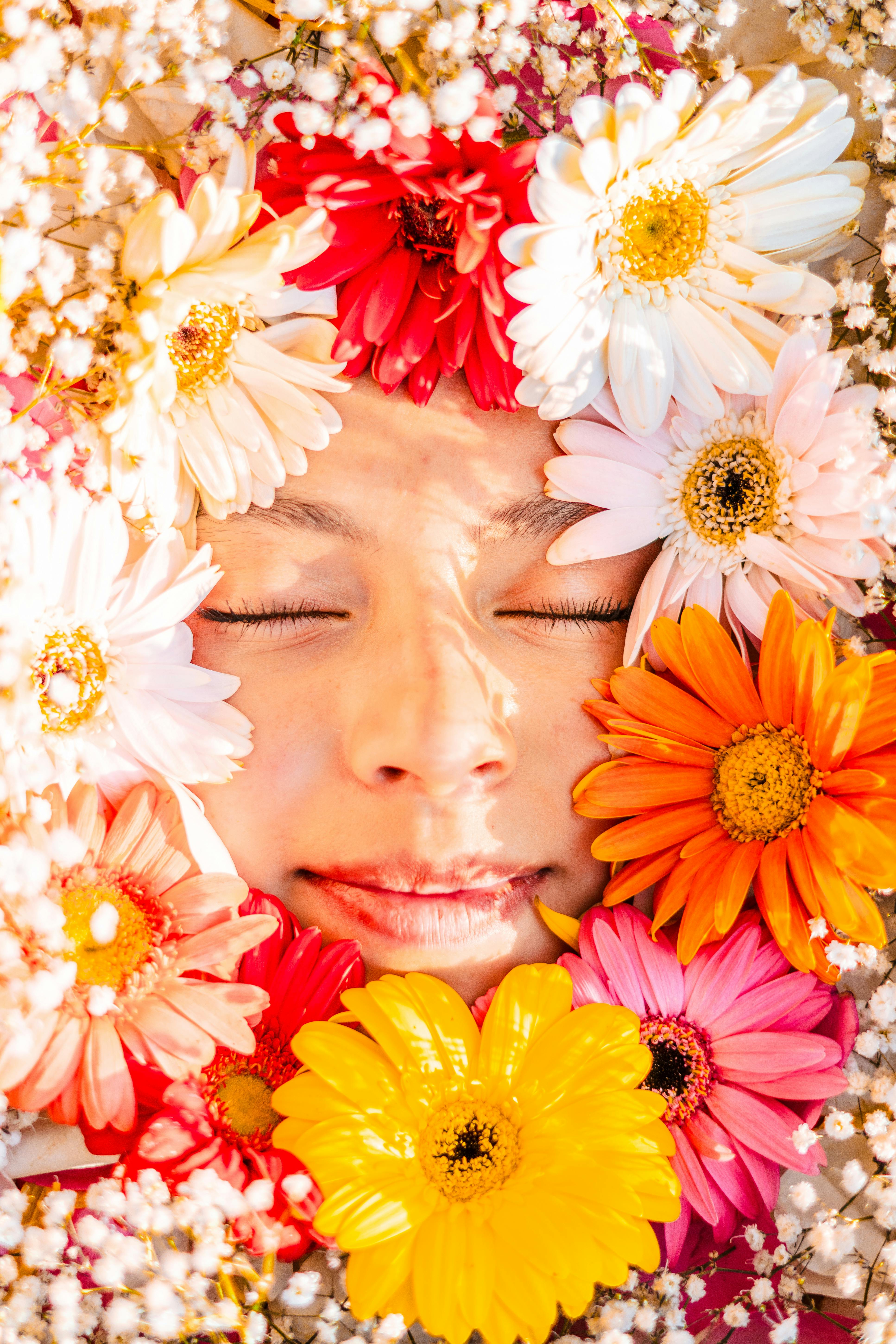 A serene face surrounded by colorful gerbera daisies, capturing spring's essence.