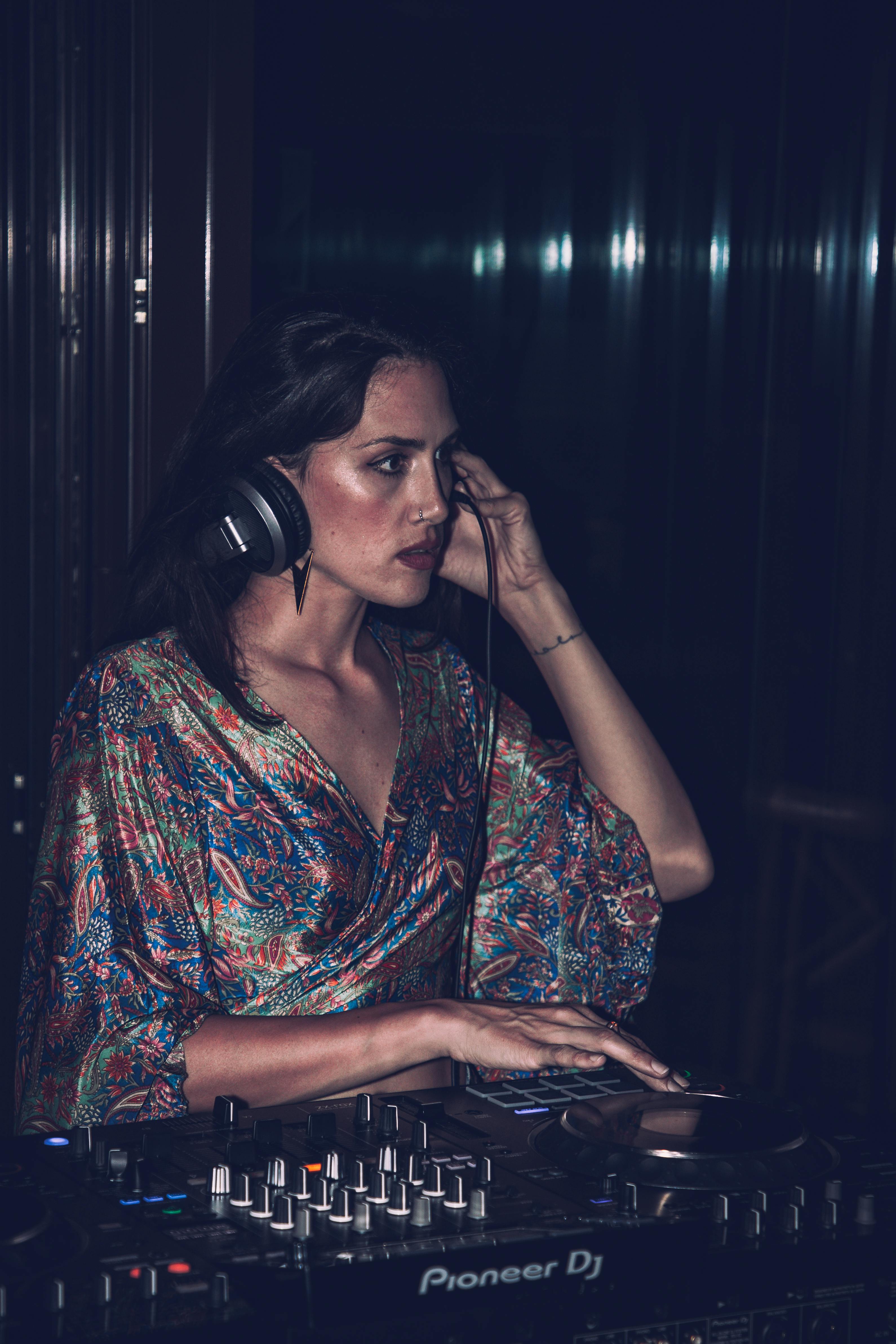 A female DJ wearing headphones, mixing music at a nightclub party.
