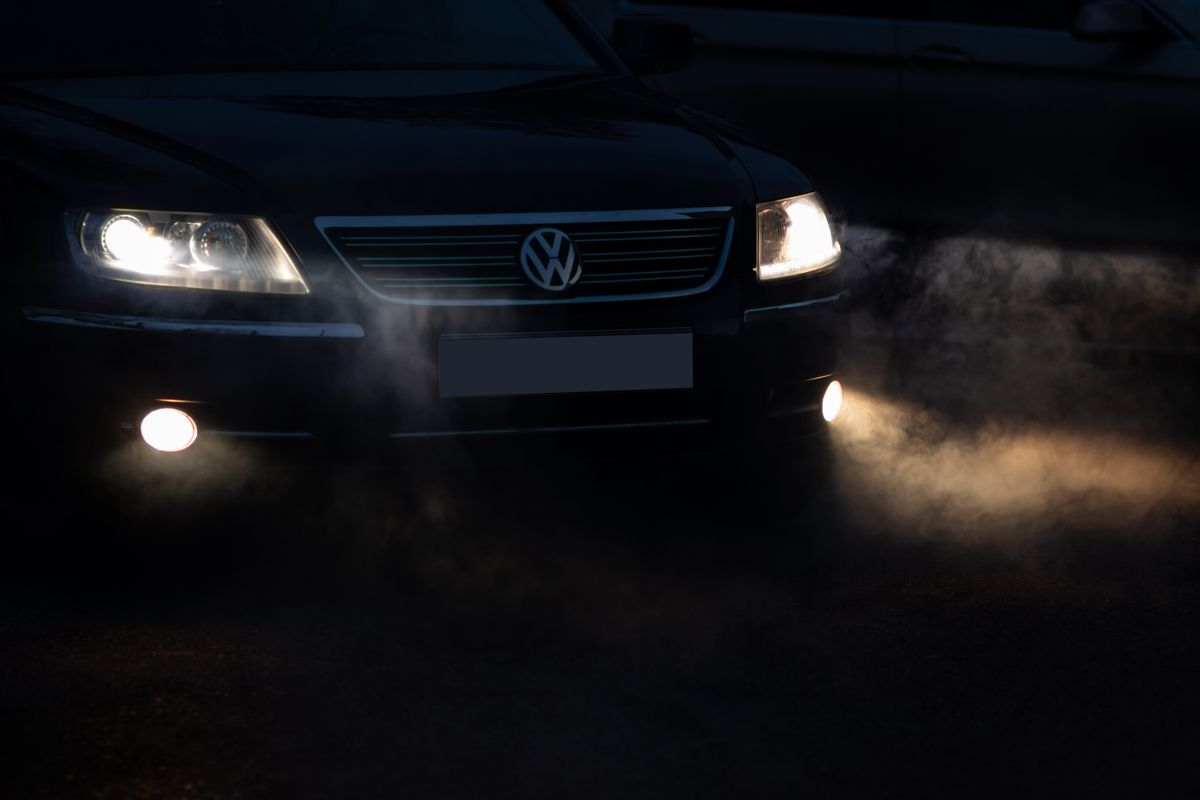 A car's headlights glowing through fog on a dark early morning