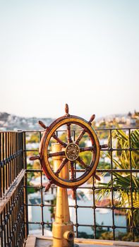 Antique wooden ship steering wheel on an outdoor deck with scenic view.