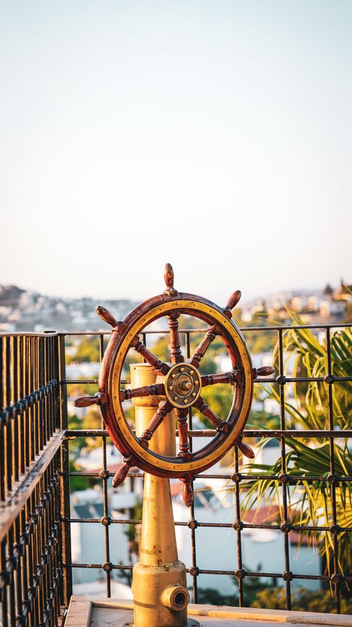 Free Antique wooden ship steering wheel on an outdoor deck with scenic view. Stock Photo