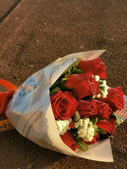 Free A beautifully wrapped bouquet of red roses with white accents on a textured ground, accentuated by warm lighting. Stock Photo