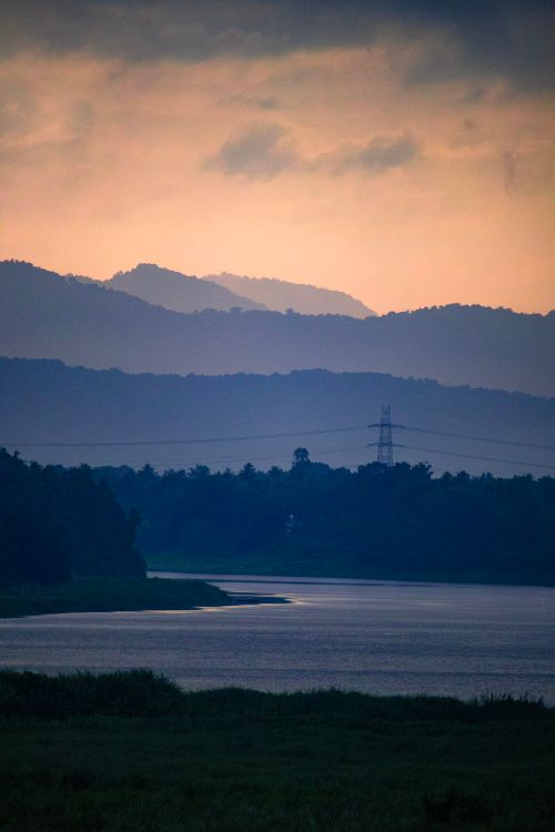 Free A peaceful landscape of a river and silhouetted mountains under a foggy dawn sky. Stock Photo