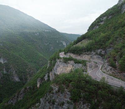 Aerial view of a winding mountain road surrounded by lush green landscape and rocky cliffs.