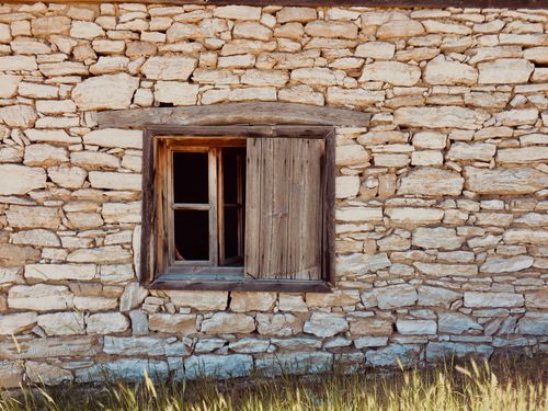 Free Weathered stone wall of a rustic cottage featuring a wooden window with open shutter Stock Photo