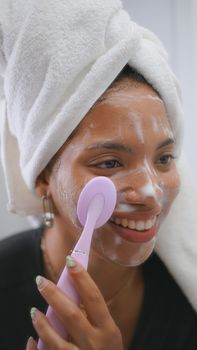 Woman applying skincare product with a tool in the bathroom, smiling and relaxed.