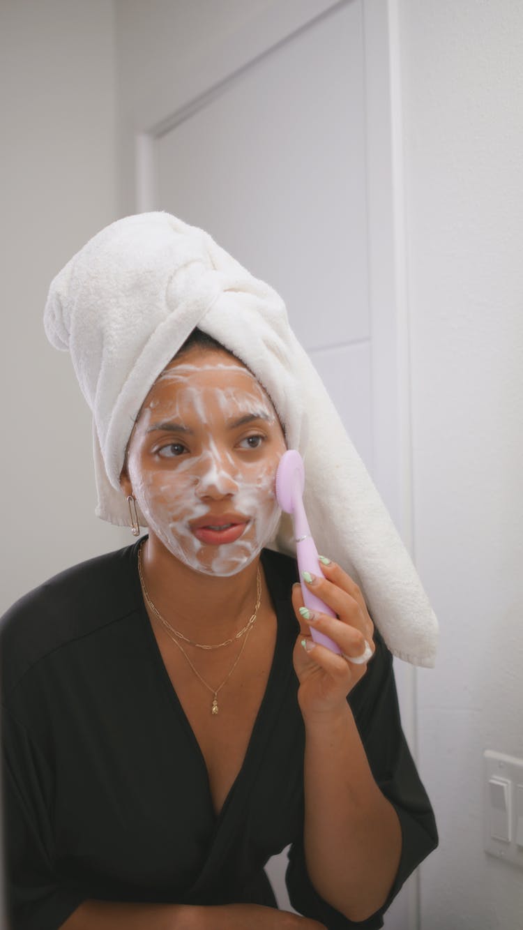 Woman In Towel On Head Looking In Mirror Doing Skincare Procedures