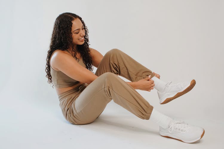 Smiling Woman In Sportswear Wearing Sneakers In Studio