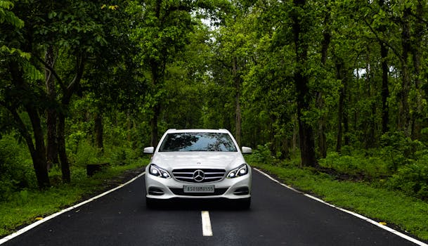 A Mercedes-Benz car driving through a lush green forest road in Guwahati, India.