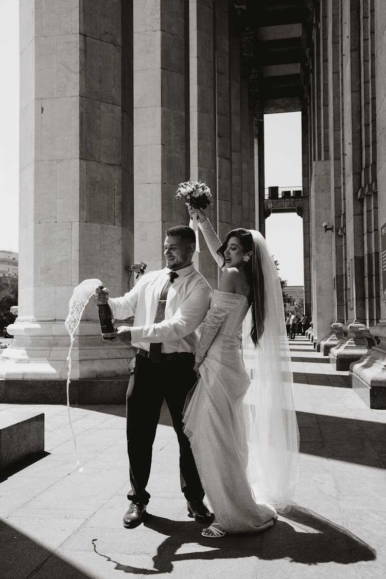 A Newlywed Couple Opening A Bottle Of Champagne