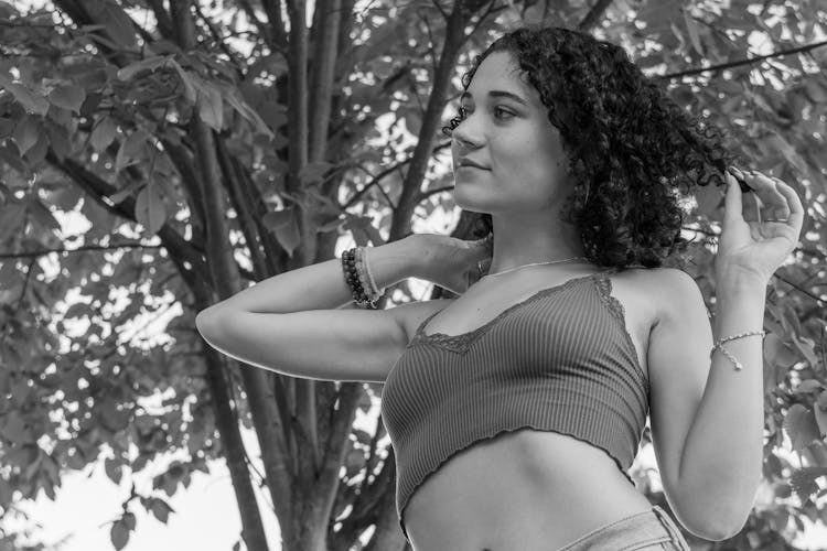 Black And White Low Angle Shot Of A Woman Wearing A Summer Blouse, Standing Against A Tree