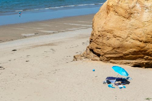 Free A serene beach scene with a vibrant blue umbrella and sandstone formation on a sunny day. Stock Photo