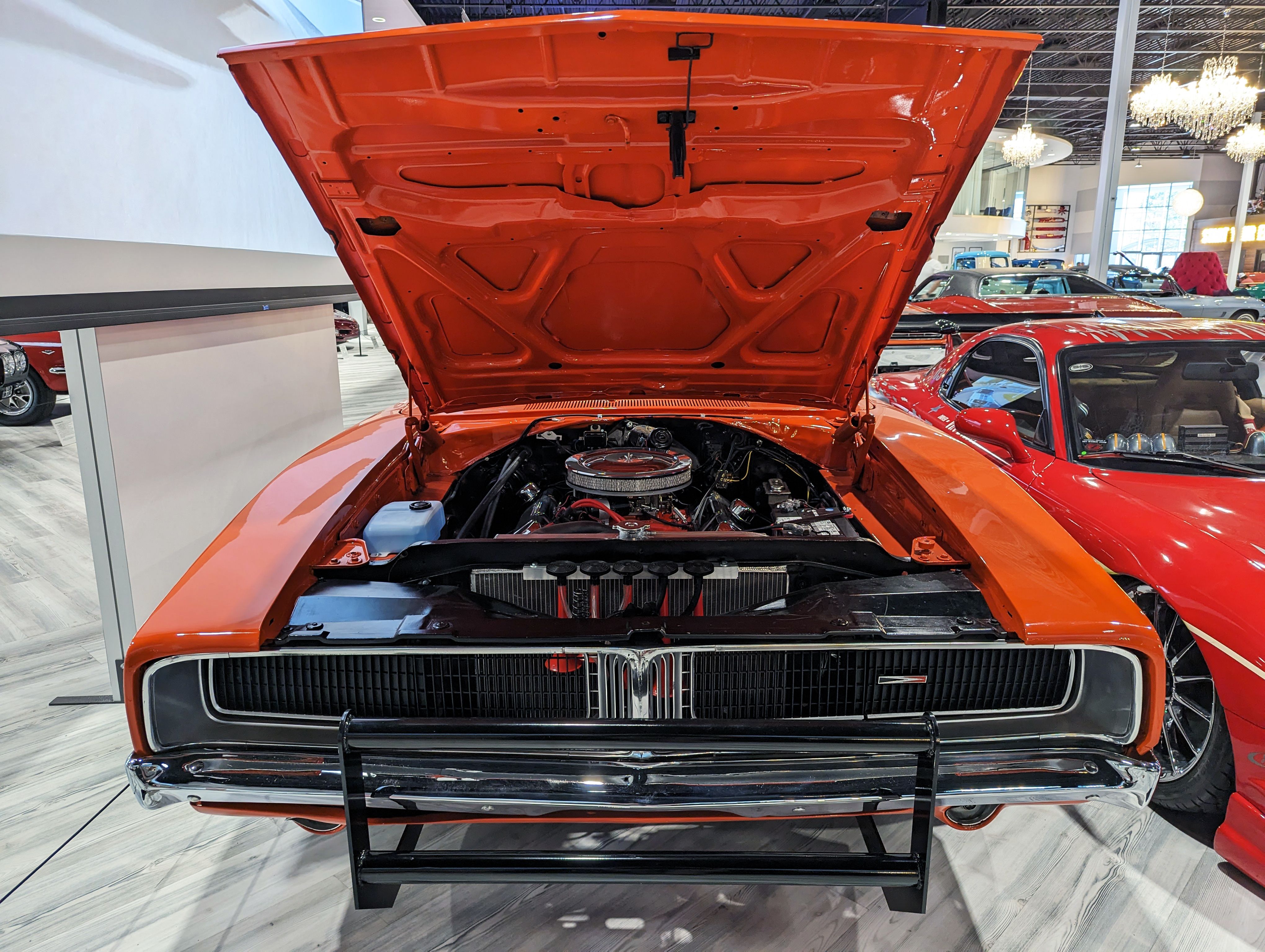 Showcase of a vintage orange Dodge Charger with its hood open, highlighting its engine.