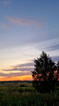 A beautiful sunset over a rural landscape with trees and an open sky.