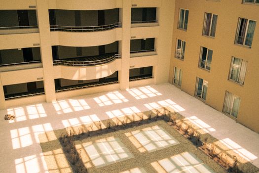 Sunlit modern apartment courtyard with geometric shadow patterns from windows.
