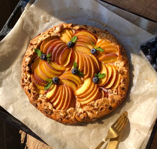 Free Sunlit rustic peach tart with blueberries on parchment, perfect for desserts and food photography. Stock Photo