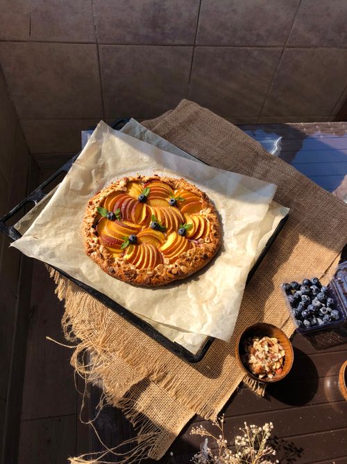 Free Delicious homemade peach tart on burlap with blueberries and nuts in warm sunlight. Stock Photo